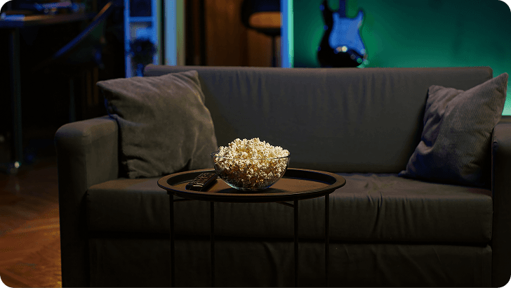 Un salón en penumbra con un sofá y un cuenco de palomitas: el cine como espacio de refugio en casa.
